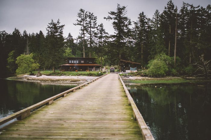 wooden bridge runs over water toward cabin in the woods