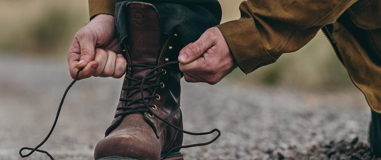 hands tying tall brown boots