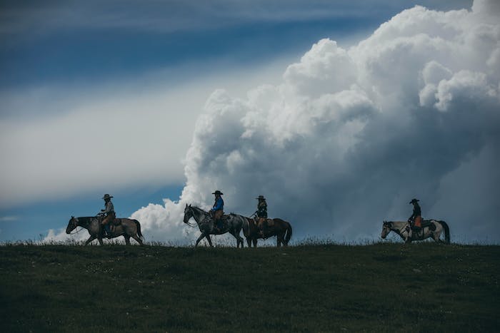 dark cloudy landscape with four horses and riders on the crest of a hill riding towards the left side of the image