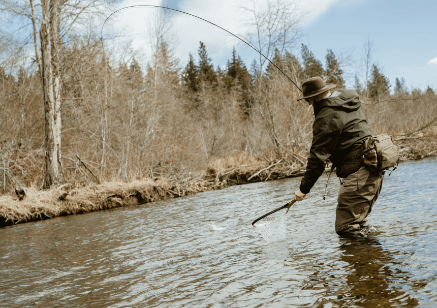 man with a fly fishing rod reeling in a fish into a fishing net