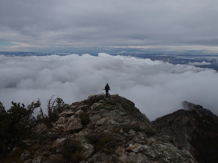 Snowcock Hunting; hunter stands on mountaintop above the clouds