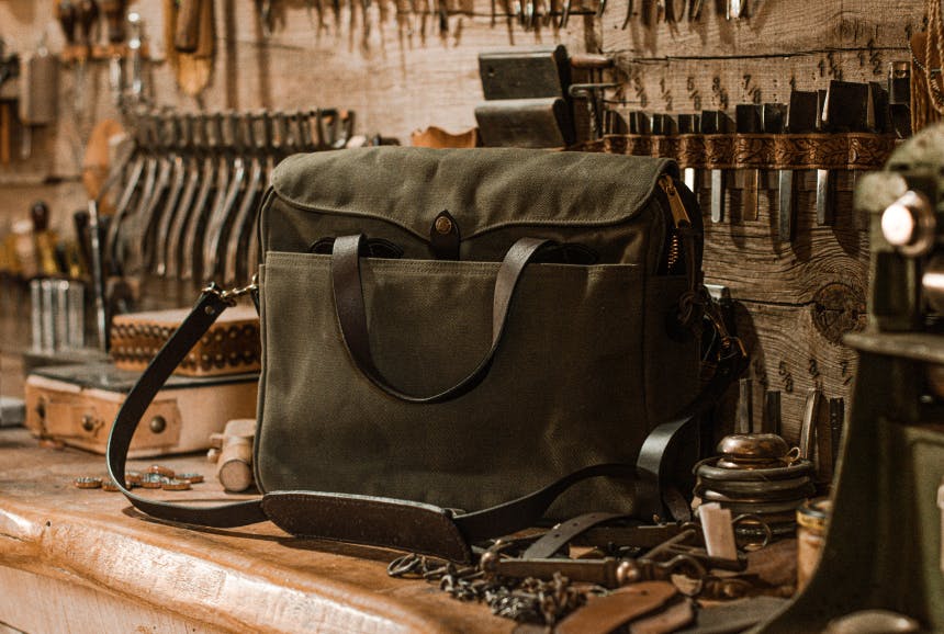 olive green filson brief case on workshop bench with many tools hanging on the wall