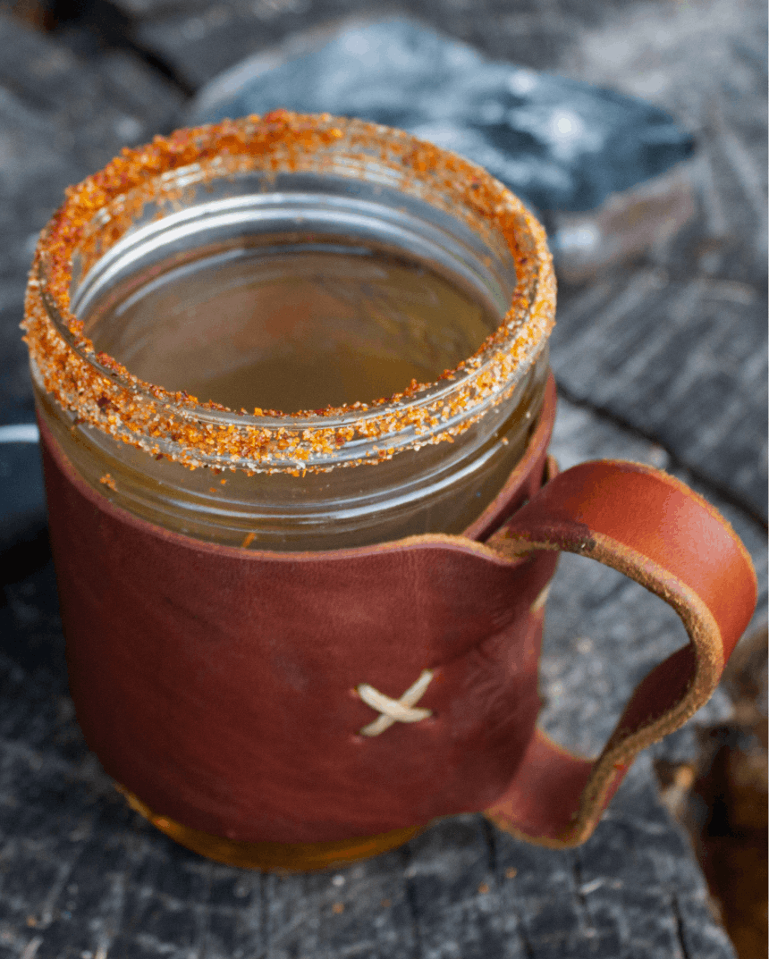 a mason jar inside a leather holder with a salted chili rim