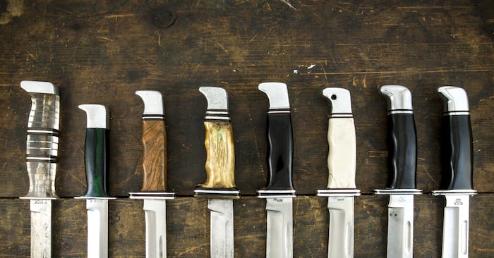 a collection of fixed blade buck knives on a table, detailing the handle materials