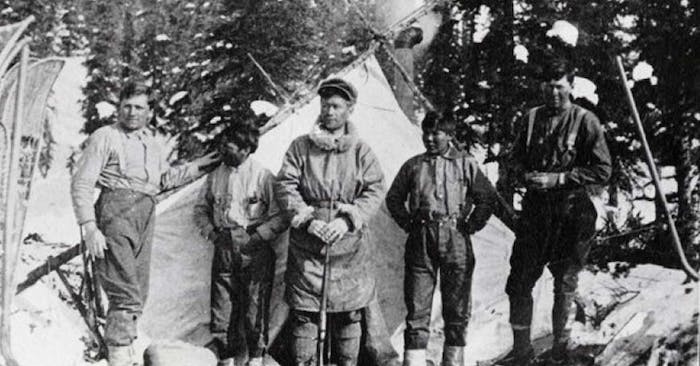 old black and white photo of men standing in front of tent in snowy forest